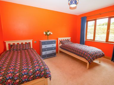 A bedroom with two beds and a chest of drawers with flowers by a window at Rossanean in Farranfore near Killarney County Kerry