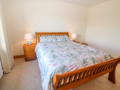 A bedroom with a wooden bed frame and floral bedding two bedside tables with lamps and a beige carpet at Rossanean in Farranfore near Killarney County Kerry