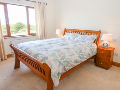 A bedroom with a wooden bed and floral bedding next to a wooden bedside table with a lamp at Rossanean in Farranfore near Killarney County Kerry
