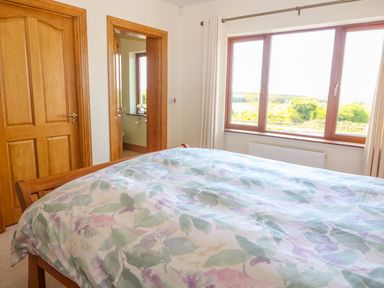 A bedroom with a wooden bed and floral bedspread windows with curtains and wooden doors at Rossanean Farranfore near Killarney County Kerry