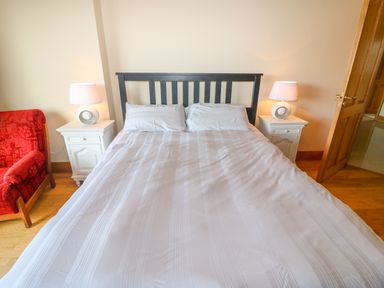 A bedroom with a double bed and two white bedside tables with lamps and a red armchair at Rossanean in Farranfore near Killarney County Kerry