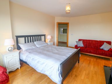 A bedroom with a black framed bed with white bedding two white bedside tables with lamps a red sofa with cushions and a wooden floor at Rossanean in Farranfore near Killarney County Kerry