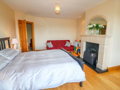 A bedroom with a large bed a red sofa and a fireplace with flowers on the mantelpiece at Rossanean in Farranfore near Killarney County Kerry