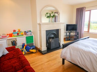 A bedroom with a bed a fireplace a red couch a toy motorcycle and a TV on a stand at Rossanean in Farranfore near Killarney County Kerry
