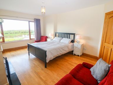 A bedroom with a black bed white bedside tables red armchairs and a large window at Rossanean Farranfore near Killarney County Kerry