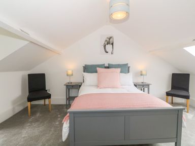 A bedroom with a gray bed frame a pink blanket two black chairs and two bedside tables with lamps at Lyngaran House in Holyhead