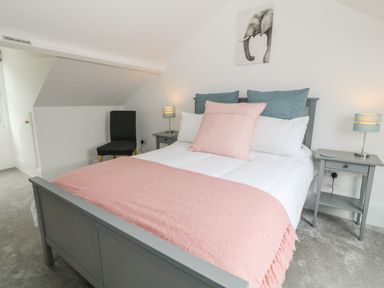 A bedroom with a gray bed frame pink blanket and pillows two gray nightstands with lamps a black chair and elephant artwork on the wall at Lyngaran House in Holyhead