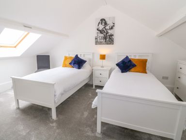 A bedroom with two white beds side by side with colorful pillows a nightstand with a lamp a chair and a skylight window at Lyngaran House in Holyhead