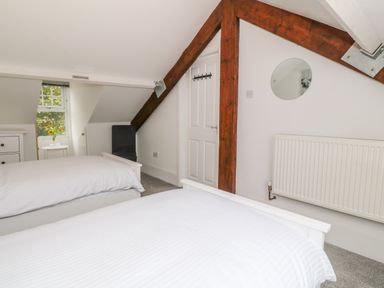 A bedroom with two beds a small window with flowers a white door and wooden beams at Lyngaran House in Holyhead