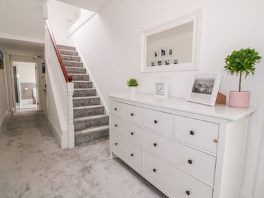A hallway with carpeted stairs a white dresser with plants and a framed picture at Lyngaran House in Holyhead