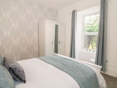 A bedroom with a bed with pillows and blue throw a white wardrobe and a window with curtains at Lyngaran House in Holyhead