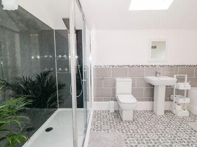 A bathroom with a shower, toilet, sink, mirror, and storage unit at Lyngaran House in Holyhead