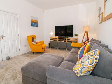 A living room with a gray sofa and yellow armchair facing a TV and wooden media console at Lyngaran House in Holyhead
