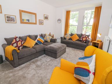 A living room with two gray sofas a yellow armchair and cushions at Lyngaran House in Holyhead