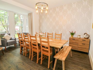 A dining room with a wooden table surrounded by chairs and a bench next to a sideboard and armchairs at Lyngaran House in Holyhead