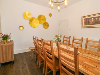 A dining room with a long wooden table surrounded by wooden chairs and a sideboard with a plant at Lyngaran House in Holyhead