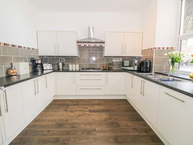 A kitchen with white cabinets black countertops and wood flooring at Lyngaran House in Holyhead