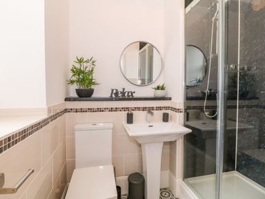 A bathroom with a toilet pedestal sink shower with glass door round mirror plants and a relax sign at Lyngaran House in Holyhead