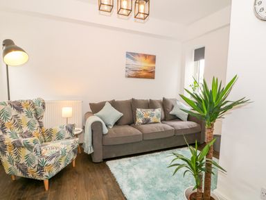 A living room with a brown sofa a patterned armchair a floor lamp and a green plant at Lyngaran House in Holyhead
