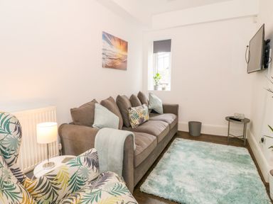 A living room with a brown sofa a patterned armchair a wall-mounted TV and a blue rug at Lyngaran House in Holyhead