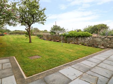 A garden with grass a tree stone wall and paved patio at Lyngaran House in Holyhead