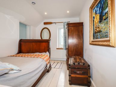 A bedroom with a wooden bed a wooden chest an armoire a round mirror and a framed painting at Blue Bay Beach House in Mawgan Porth