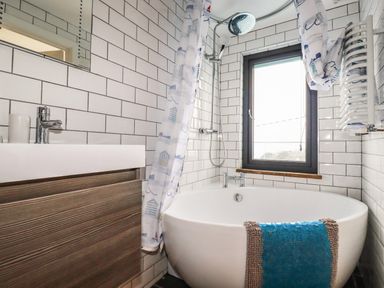 A bathroom with a bathtub shower combination a sink and a window at Blue Bay Beach House in Mawgan Porth