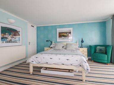 A bedroom with a bed two bedside tables with lamps a green armchair and Cornwall posters on the walls at Blue Bay Beach House in Mawgan Porth