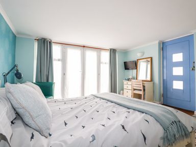 A bedroom with a bed a chair a desk with a mirror and a blue door at Blue Bay Beach House in Mawgan Porth