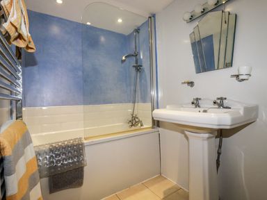 A bathroom with a bathtub shower combination towels and a pedestal sink with mirrors at Blue Bay Beach House in Mawgan Porth