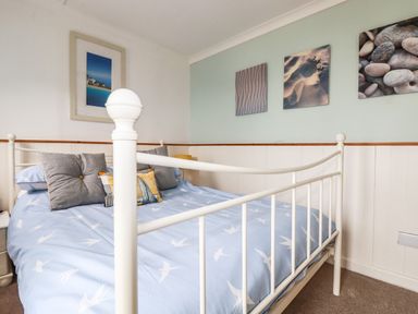 A bedroom with a white metal bed frame and blue bedding with bird patterns at Blue Bay Beach House in Mawgan Porth