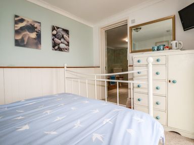 A bedroom with a bed sheet, dresser with mirror, and an open door to a bathroom at Blue Bay Beach House in Mawgan Porth