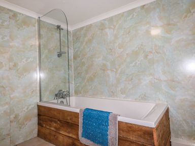 A bathroom with a bathtub wood-paneled on the outside and a blue and gray towel hanging at Blue Bay Beach House in Mawgan Porth