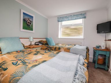 A bedroom with two single beds blue pillows and blankets a framed picture a window and a wall-mounted television at Blue Bay Beach House in Mawgan Porth