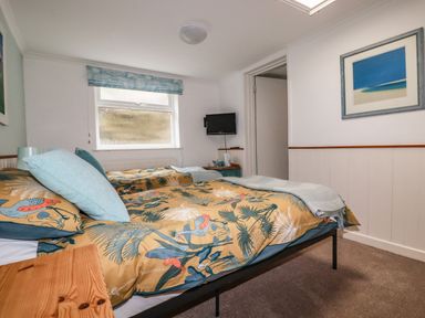 A bedroom with two single beds a window and a wall-mounted television at Blue Bay Beach House in Mawgan Porth