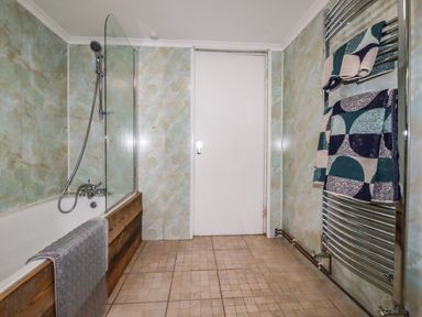 A bathroom with a bathtub shower combination a towel rack with towels and a closed door at Blue Bay Beach House in Mawgan Porth