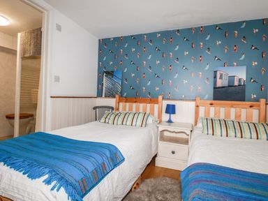 A bedroom with two single beds a nightstand with a lamp and an open door to a bathroom at Blue Bay Beach House in Mawgan Porth