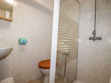 A bathroom with a toilet with wooden seat a glass shower enclosure and a sink at Blue Bay Beach House in Mawgan Porth