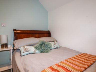 A bedroom with a wooden bed frame pillows a lamp on a small bedside table and an orange striped blanket at Blue Bay Beach House in Mawgan Porth