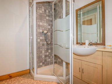 A bathroom with a corner shower and a sink with mirror at Blue Bay Beach House in Mawgan Porth