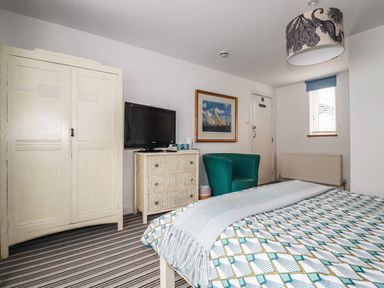 A bedroom with a bed striped carpet a wardrobe a chest of drawers with a television and a green chair at Blue Bay Beach House in Mawgan Porth
