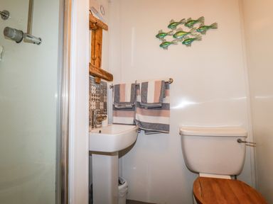 A bathroom with a shower, pedestal sink, toilet with wooden seat, striped towels, and fish wall decoration at Blue Bay Beach House in Mawgan Porth