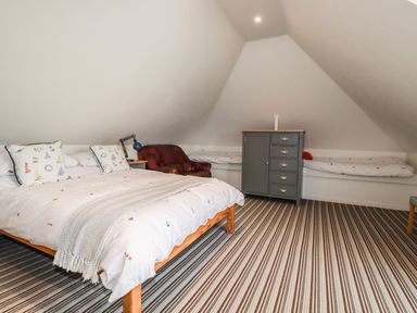 A bedroom with a double bed and a built in single bed with a striped carpet a cabinet and a chair at Blue Bay Beach House in Mawgan Porth
