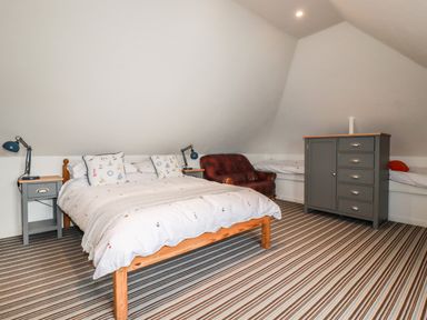 A bedroom with a double bed two bedside tables a red leather chair a gray dresser and a striped carpet at Blue Bay Beach House in Mawgan Porth