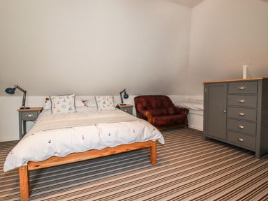 A bedroom with a bed two bedside tables with lamps a leather chair a small single bed and a grey dresser at Blue Bay Beach House in Mawgan Porth