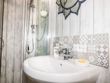 A bathroom sink with soap and toothbrush holder and a shower area with glass door at Blue Bay Beach House in Mawgan Porth