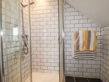 A shower area with glass doors white subway tiles and a towel on a wall-mounted radiator at Blue Bay Beach House in Mawgan Porth