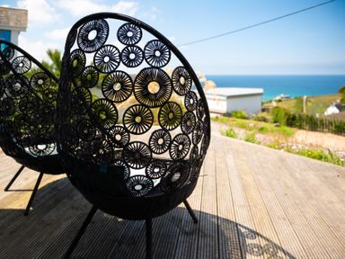 Black circular patterned outdoor chairs on a wooden deck with ocean view at Blue Bay Beach House in Mawgan Porth