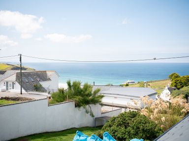 A garden area with plants and a white wall overlooking neighboring houses and the ocean at Blue Bay Beach House in Mawgan Porth