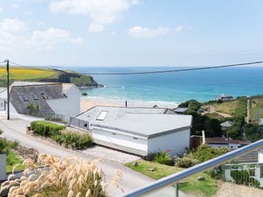 A view of houses overlooking a beach and ocean with cliffs and greenery at Blue Bay Beach House in Mawgan Porth